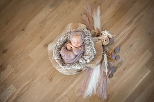 Overhead view of a sleeping baby in a cozy round basket with feather decorations on wooden floor.