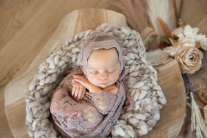 Newborn baby sleeping peacefully on soft cotton floral backdrop in neutral tones during professional photo session.