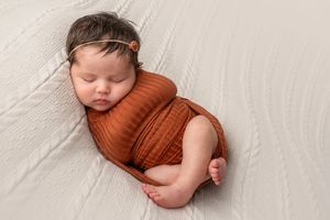 Sleeping newborn wrapped in dark gray fabric on black background in artistic pose.