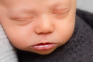 Close-up newborn photography showing tiny details and soft skin tones against a dark background.