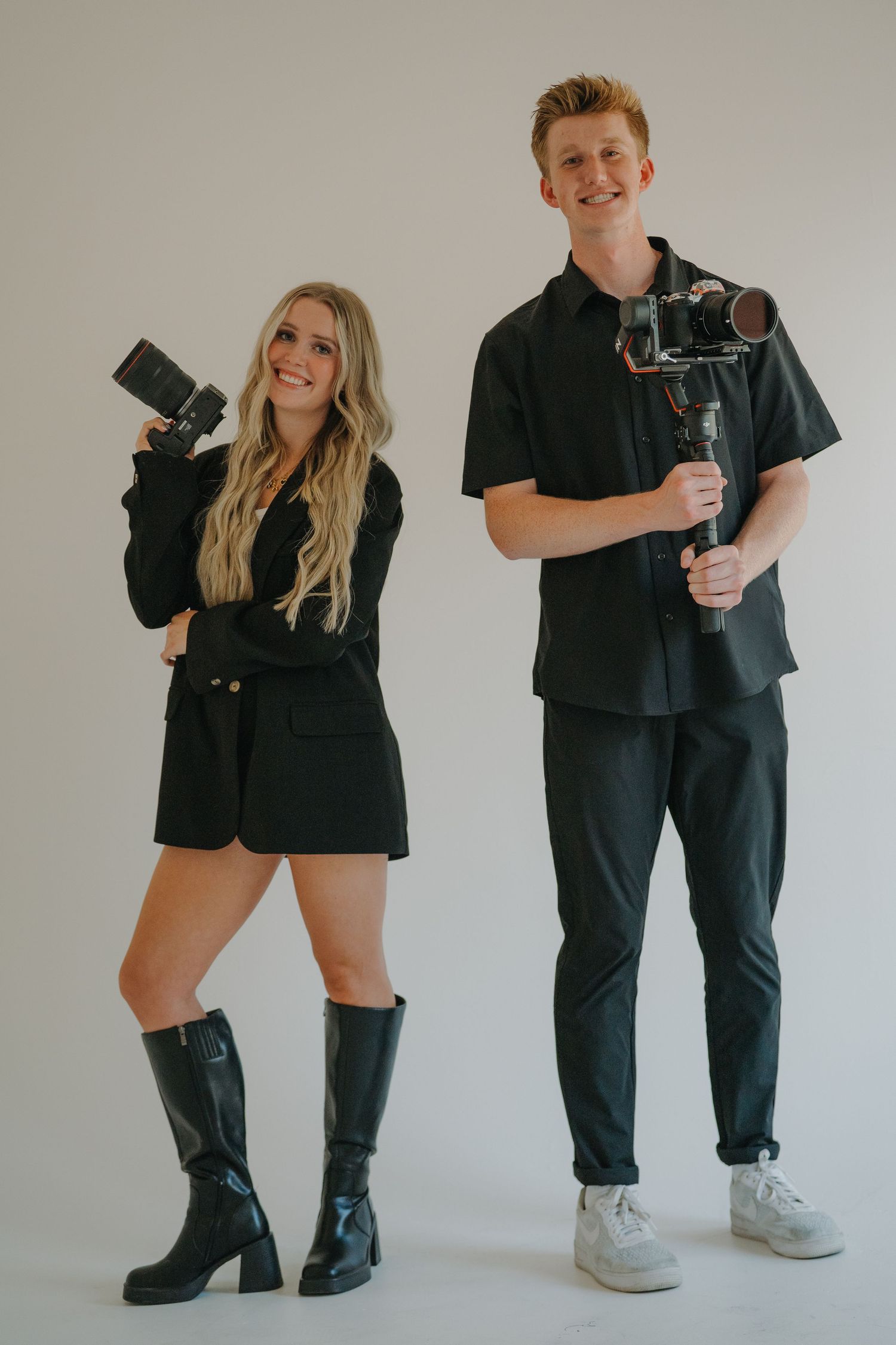 Male and female photographers in black outfits holding professional camera and gimbal stabilizer.