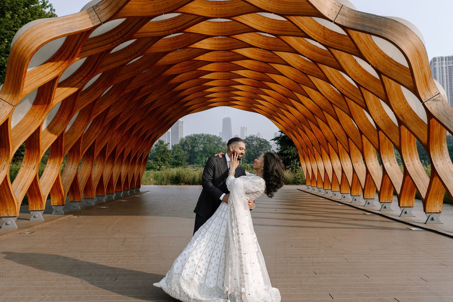 A couple poses under a geometric wooden tunnel structure with warm-toned architectural details at Lincoln Park.