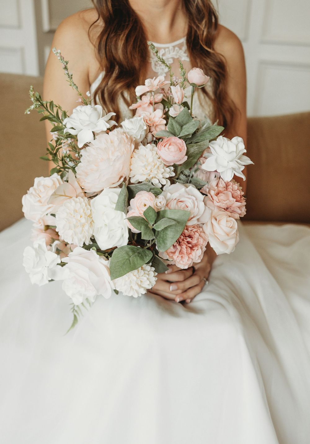 Elegant bridal bouquet with pink and white flowers against white wedding dress.