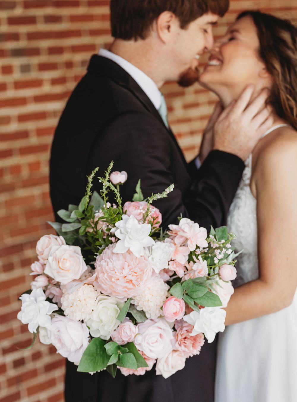 Romantic wedding portrait with pink and white floral bouquet against brick wall.