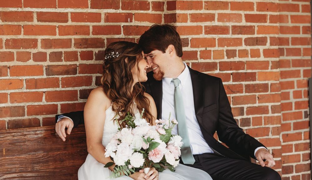 Wedding party members pose against a rustic brick wall backdrop with natural lighting.