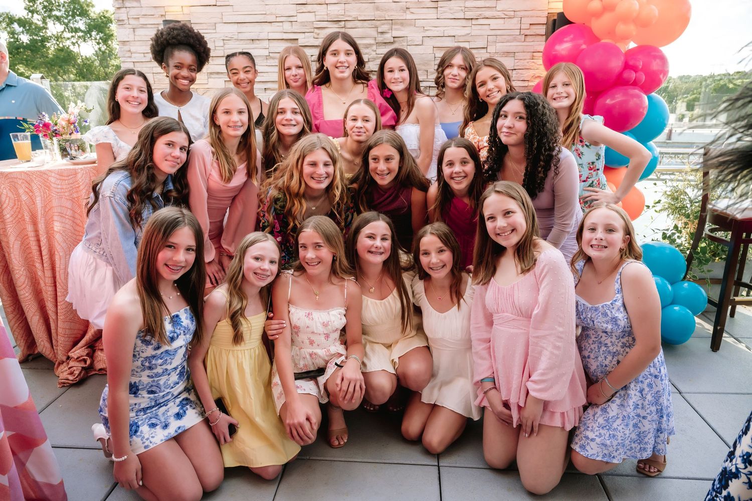 Large group celebrating outdoors wearing pink and floral summer outfits.