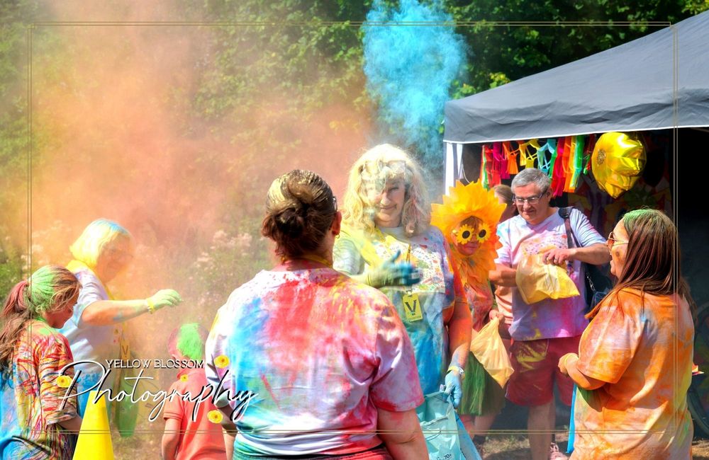 Colorful powder fills the air as participants enjoy a festive outdoor celebration under a tent.