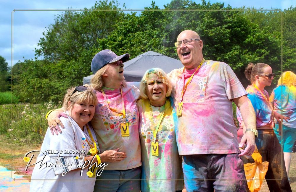 People covered in bright powder paint share laughter and hugs during an outdoor color festival.