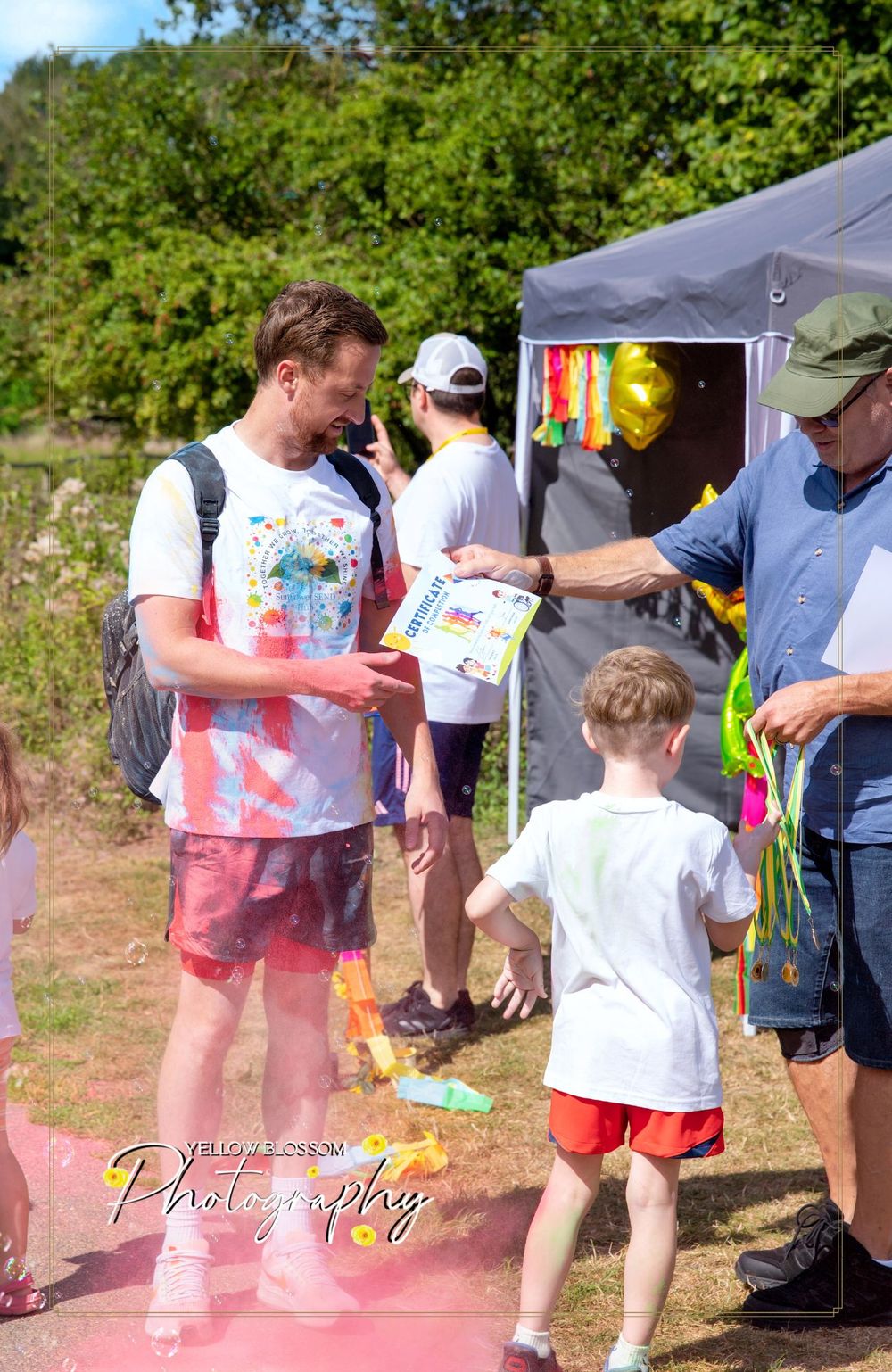 Participants covered in colorful powder visit a registration tent at an outdoor event.
