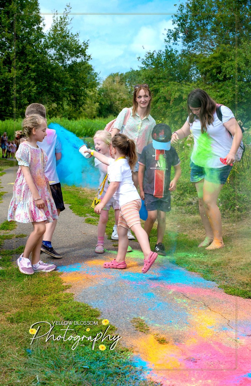 People playing in colorful powder paint during an outdoor festival on a rainbow-covered pathway.