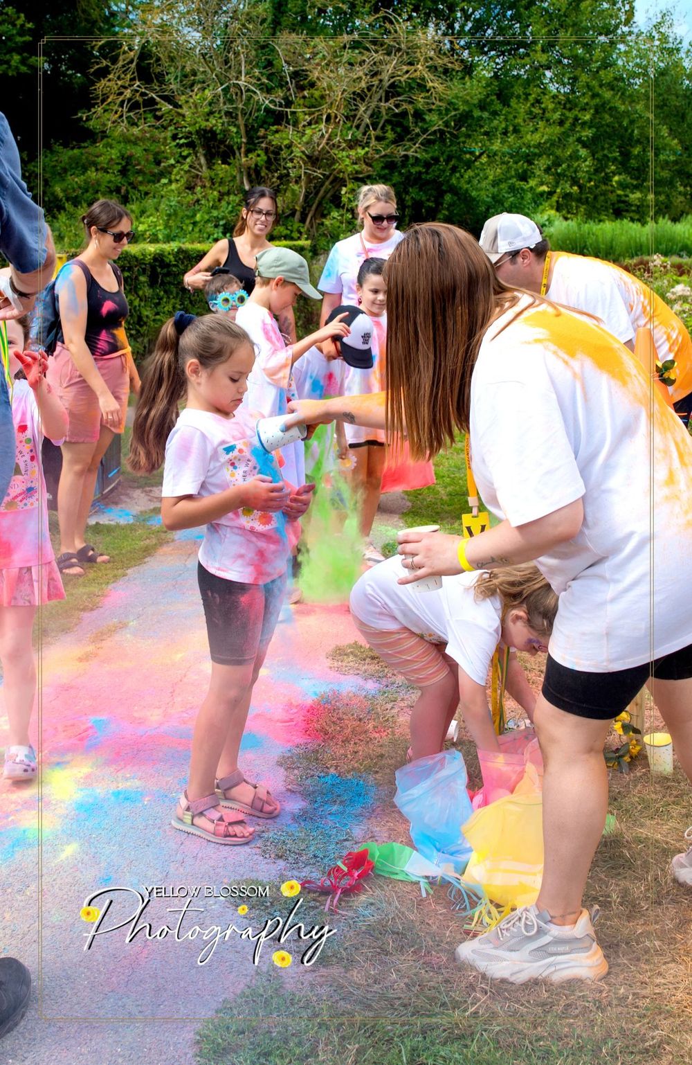 Participants at a color run event throw vibrant powder while playing outdoors in a lively summer celebration.