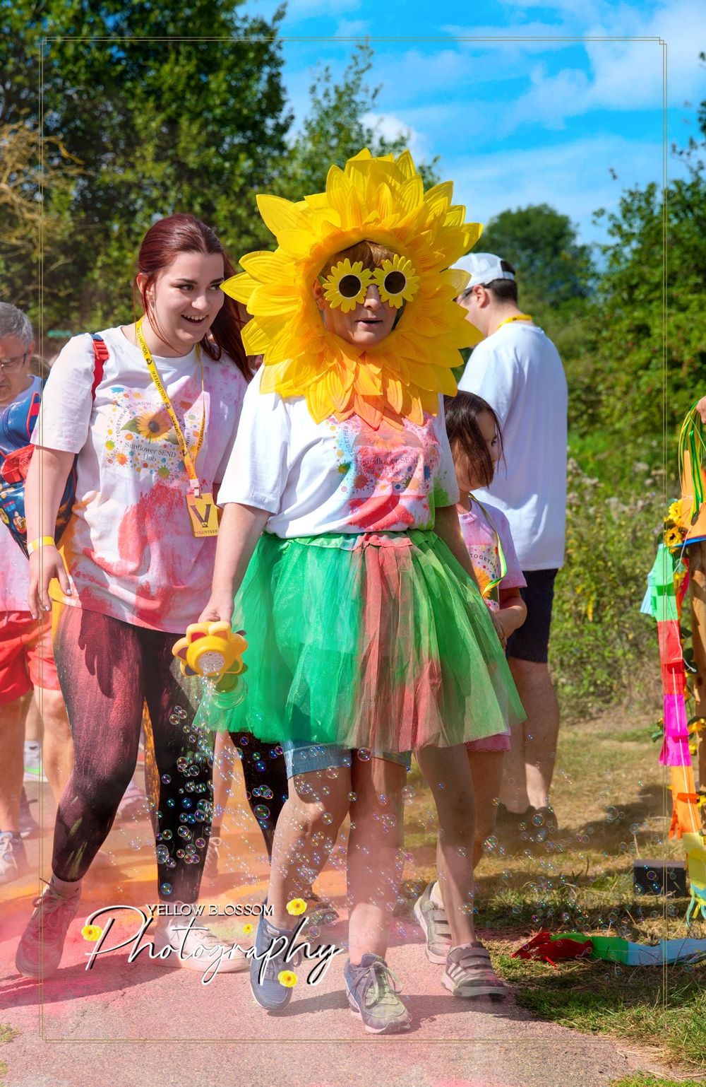 Colorful festival participants covered in powder paint including someone in a vibrant sunflower-themed costume with tutu.