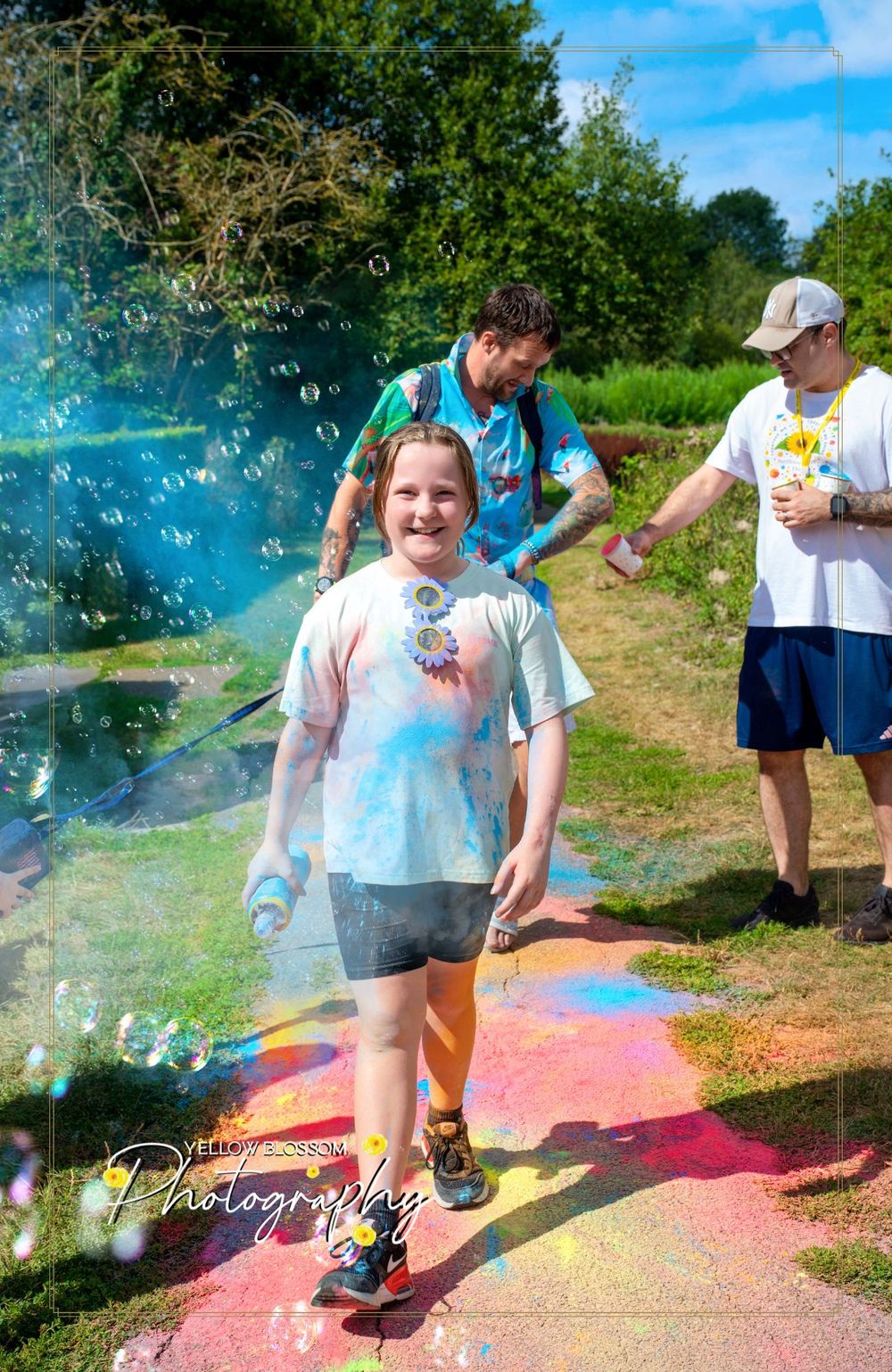 Soap bubbles float through the air at an outdoor summer event with colorful powder on the ground.