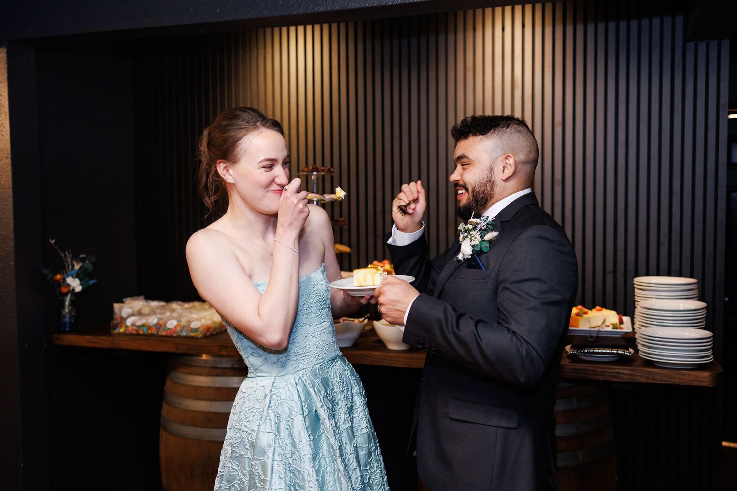 A bride and groom playfully taste cheesecake at their wedding