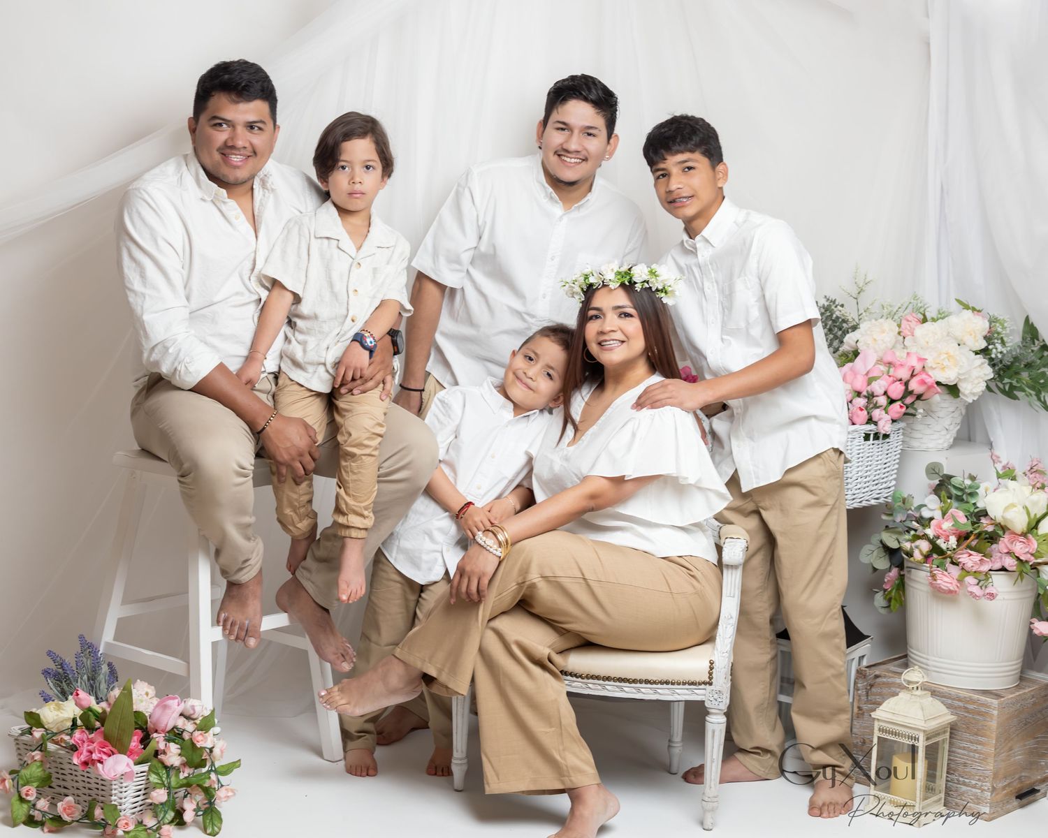 A family in coordinated white and tan outfits poses together for professional portraits on a white background with flowers.