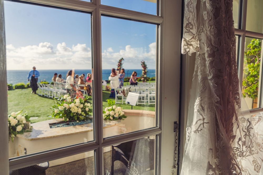White wedding dress hanging in a window with natural light and beach views in the background.