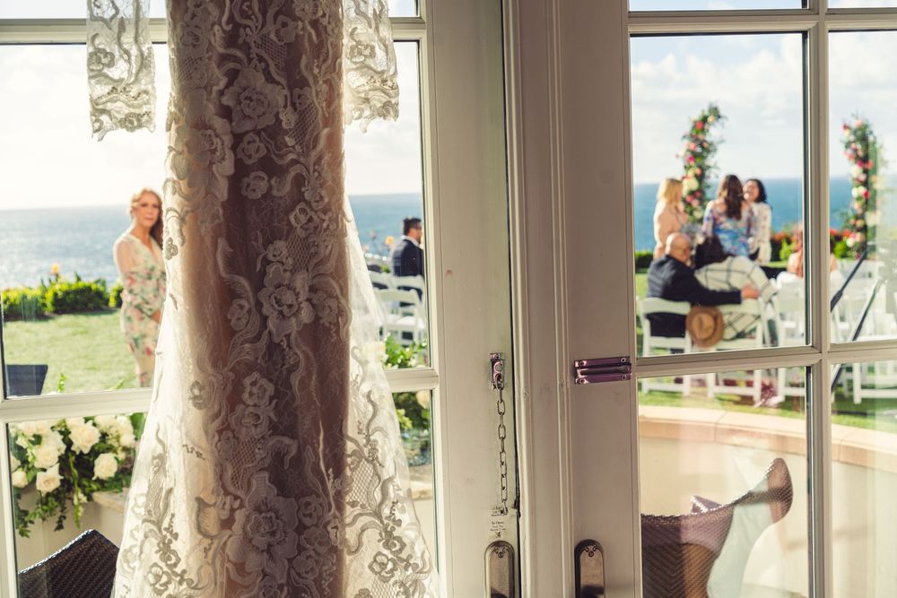 Elegant white-draped venue with ocean views through large windows and floral decorations for a wedding ceremony.