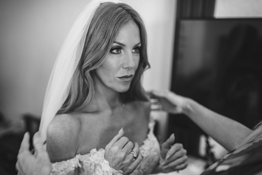 A bride in a white lace dress gets ready on her wedding day in black and white photography.