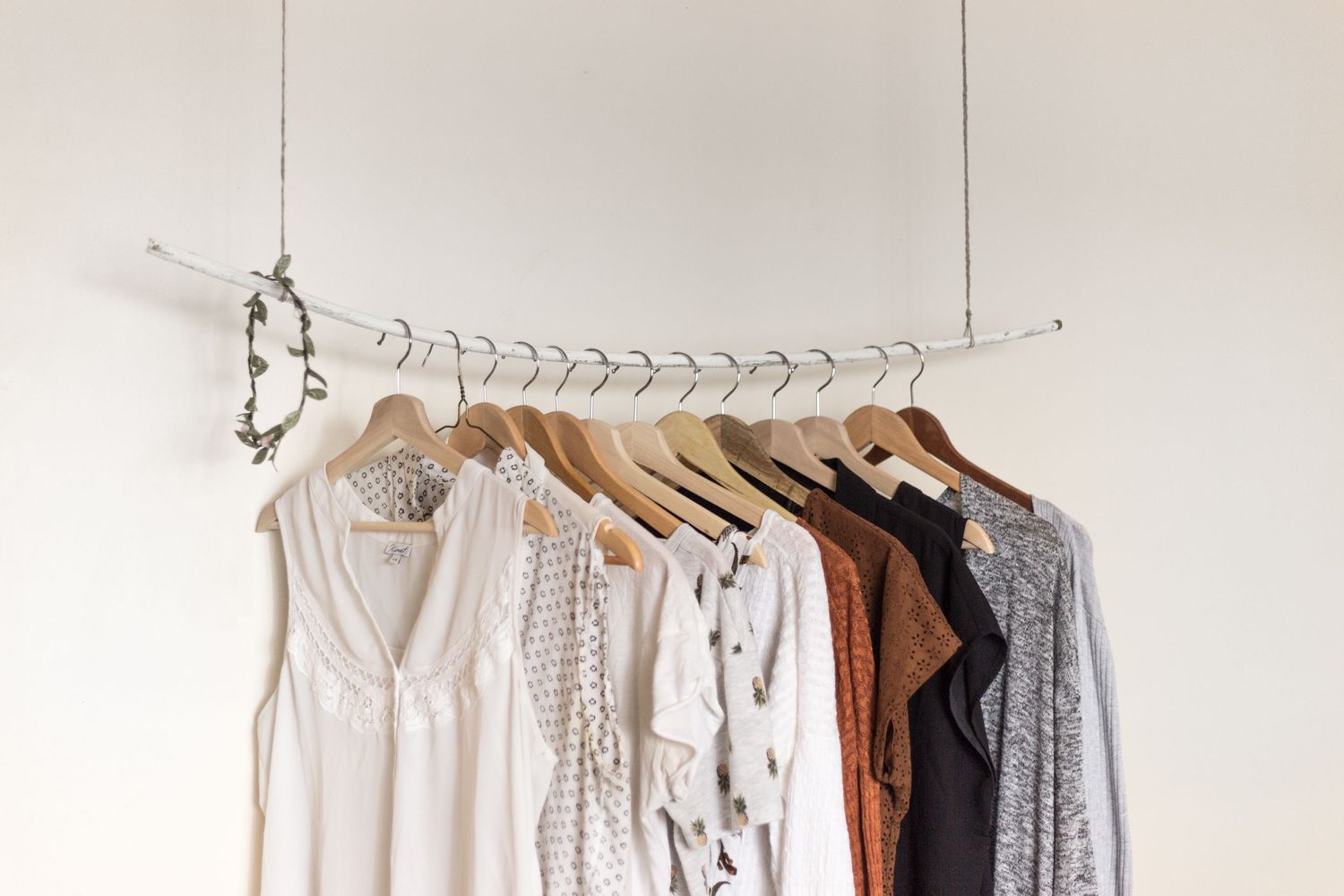 Row of light colored clothing hanging on wooden hangers against a white wall.