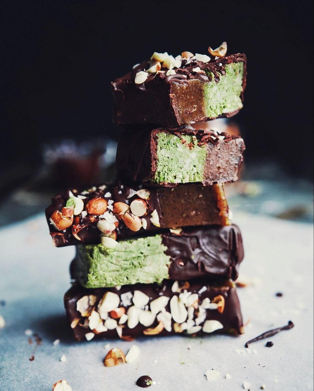 Raw chokladbitar med matcha och hasselnötter uppradade i ett torn med naturligt ljus från sidan