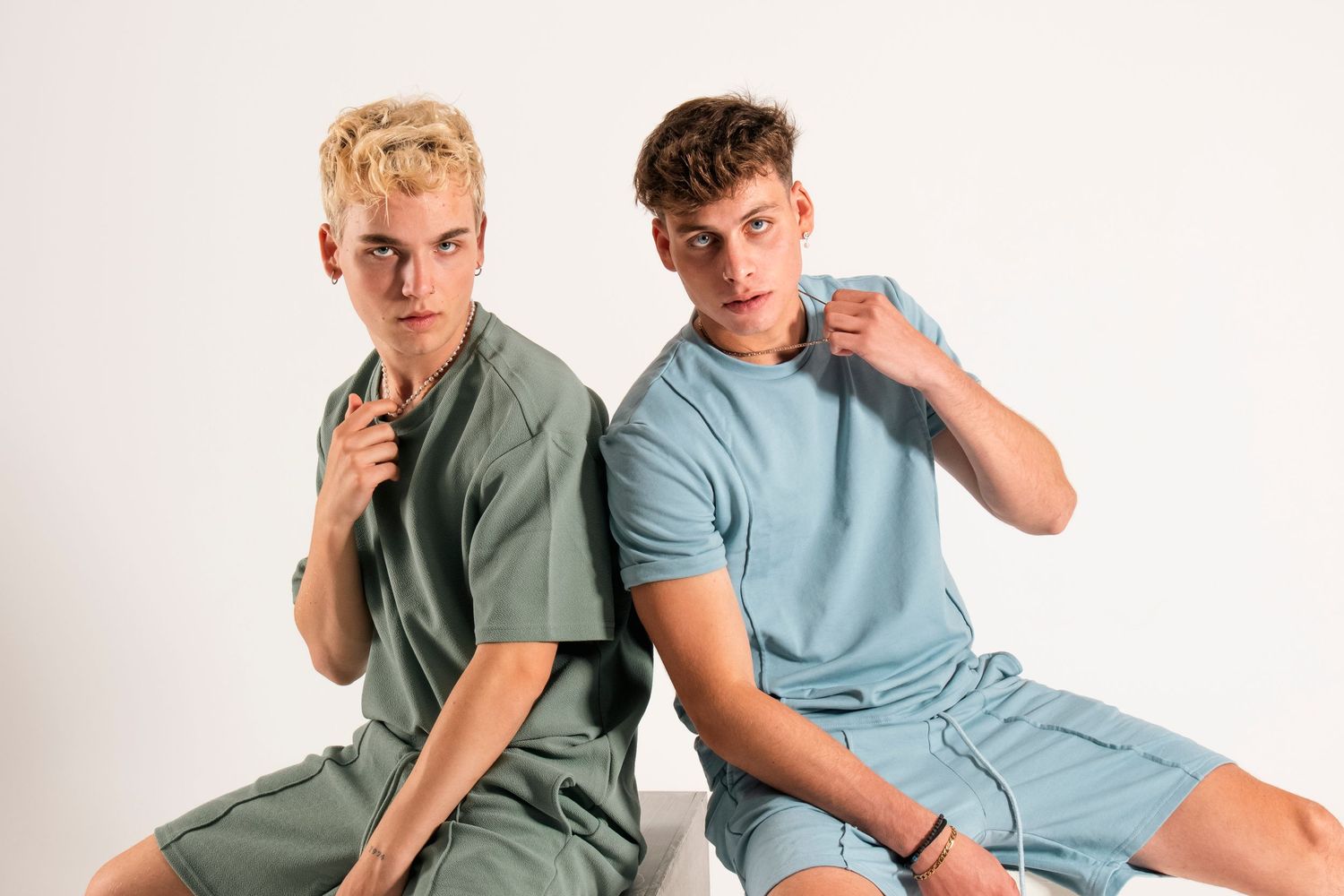 Two models in coordinated sage green and light blue casual wear posing against white backdrop.