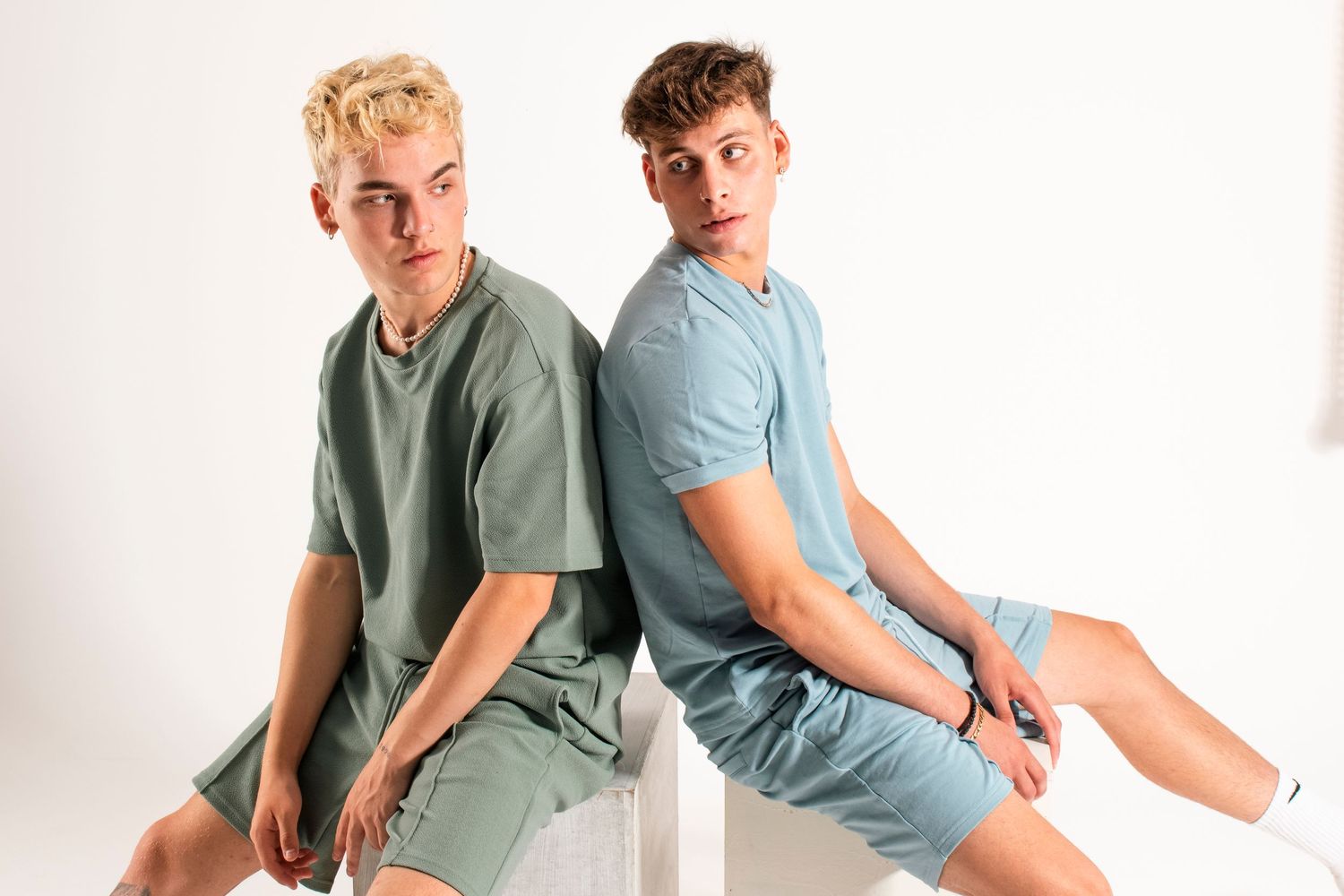 Models in sage and blue monochromatic outfits posing on white platform.