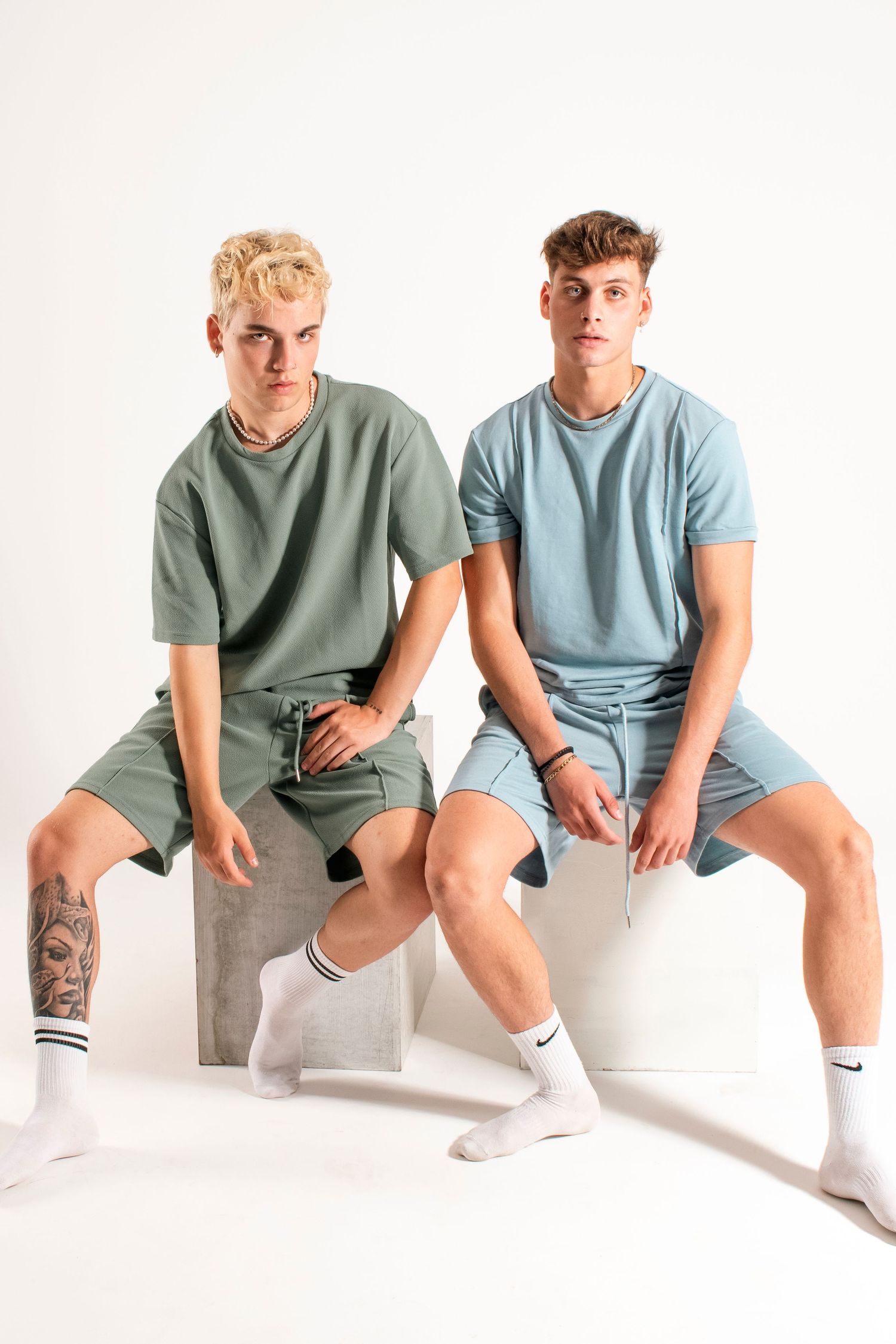 Two models wearing coordinated t-shirts and shorts sitting casually on white platform.