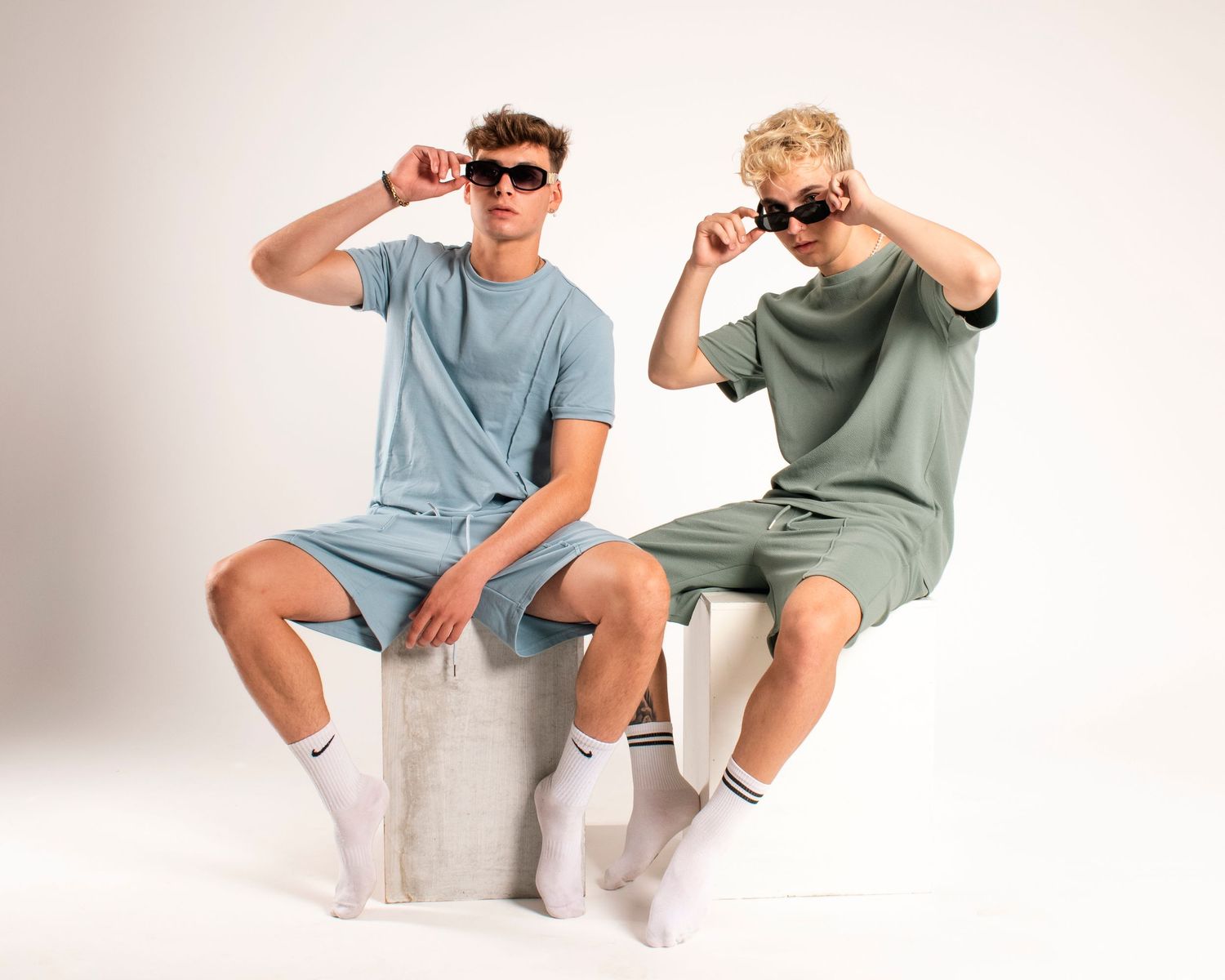 Two models in coordinated outfits wearing sunglasses and striking casual poses.