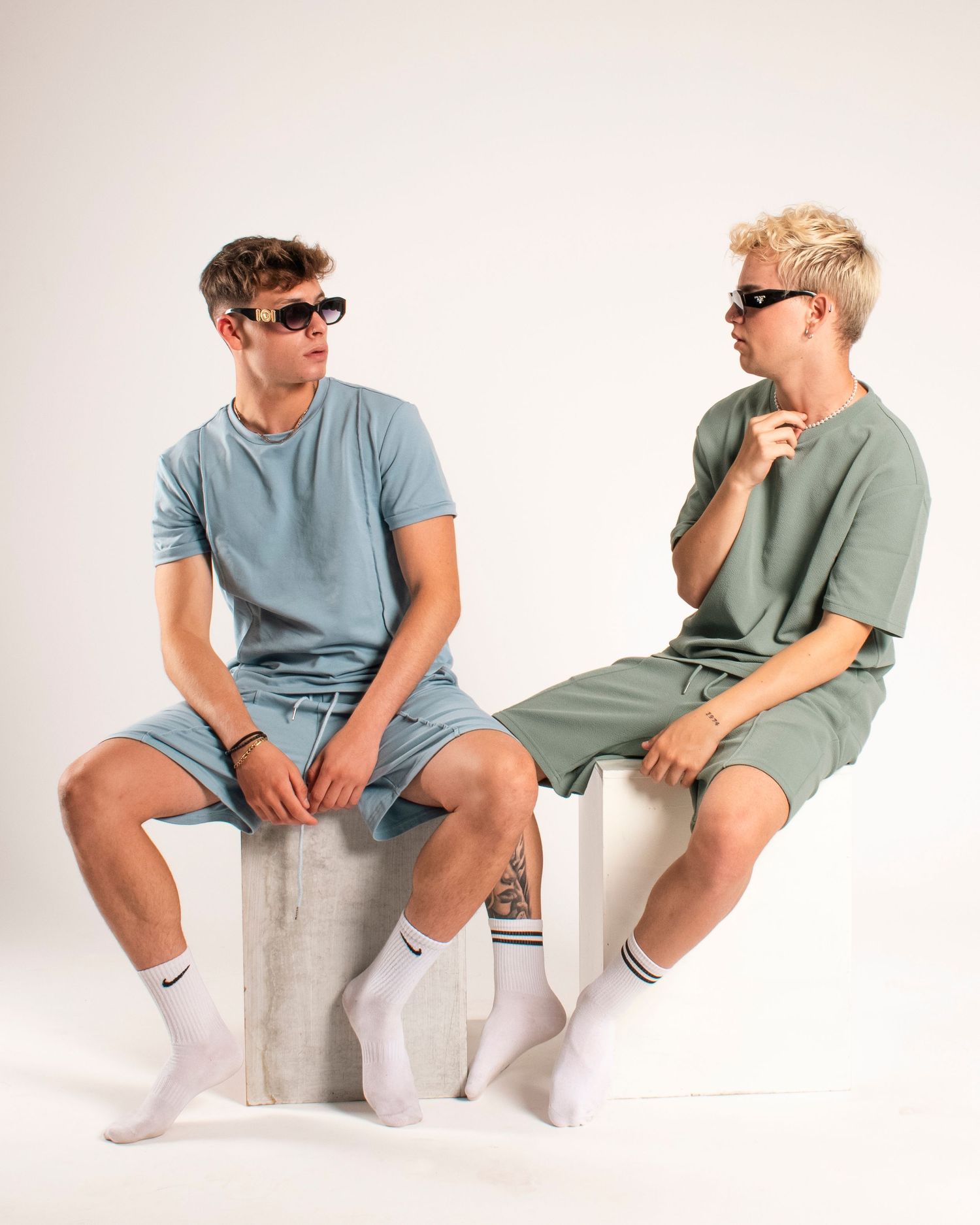 Models wearing sunglasses and coordinated casual outfits posing on white platform.