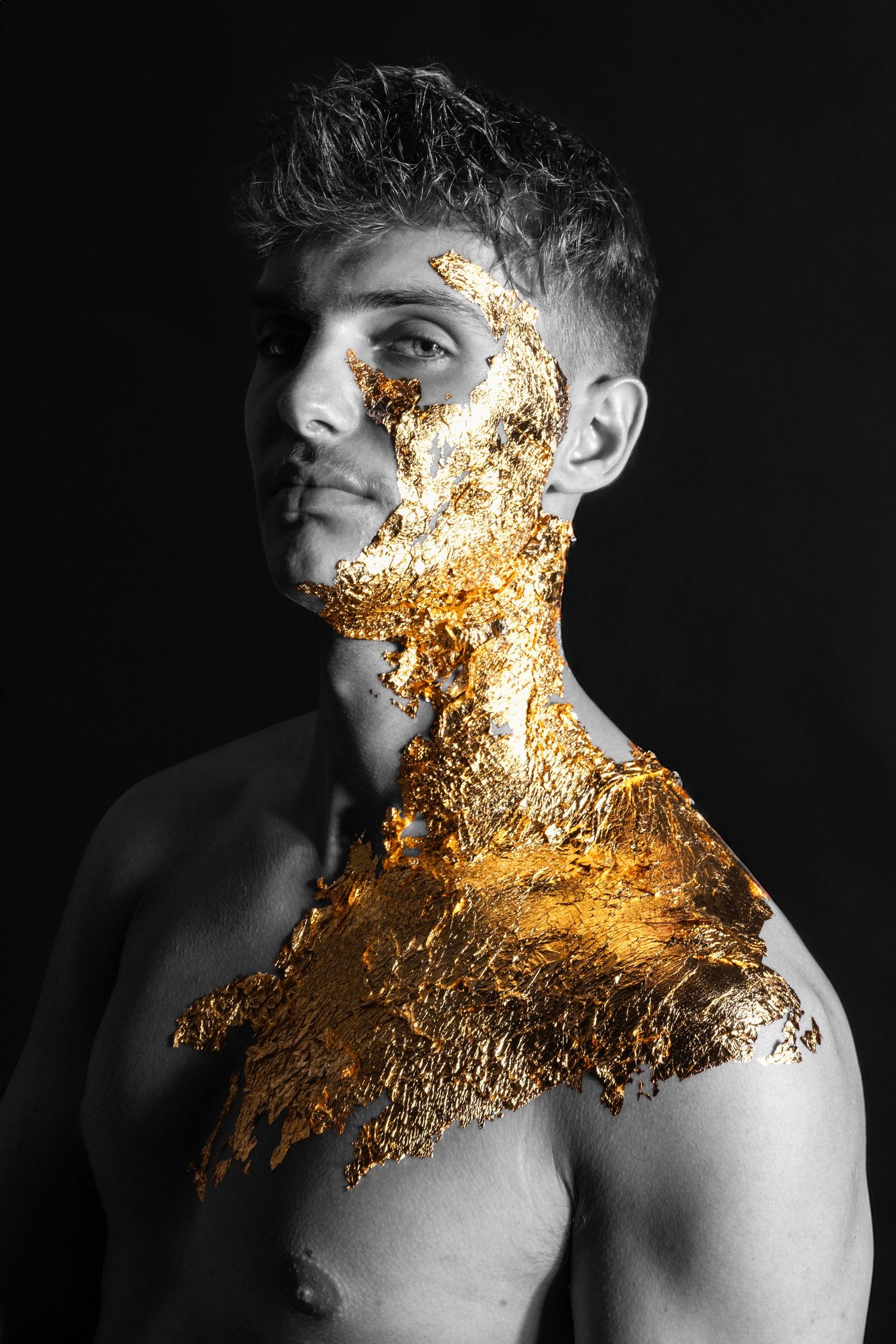 Monochromatic portrait with golden metallic paint effect on shoulder and face against dark background.