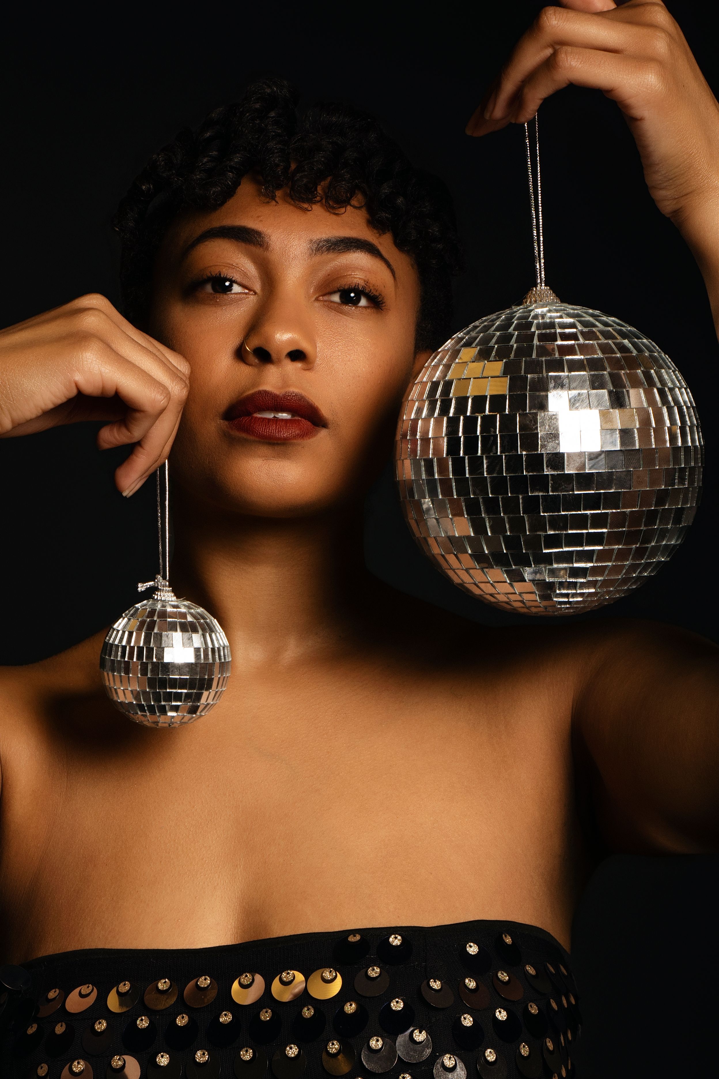 Glamorous portrait with disco ball and sequined dress in dark setting.