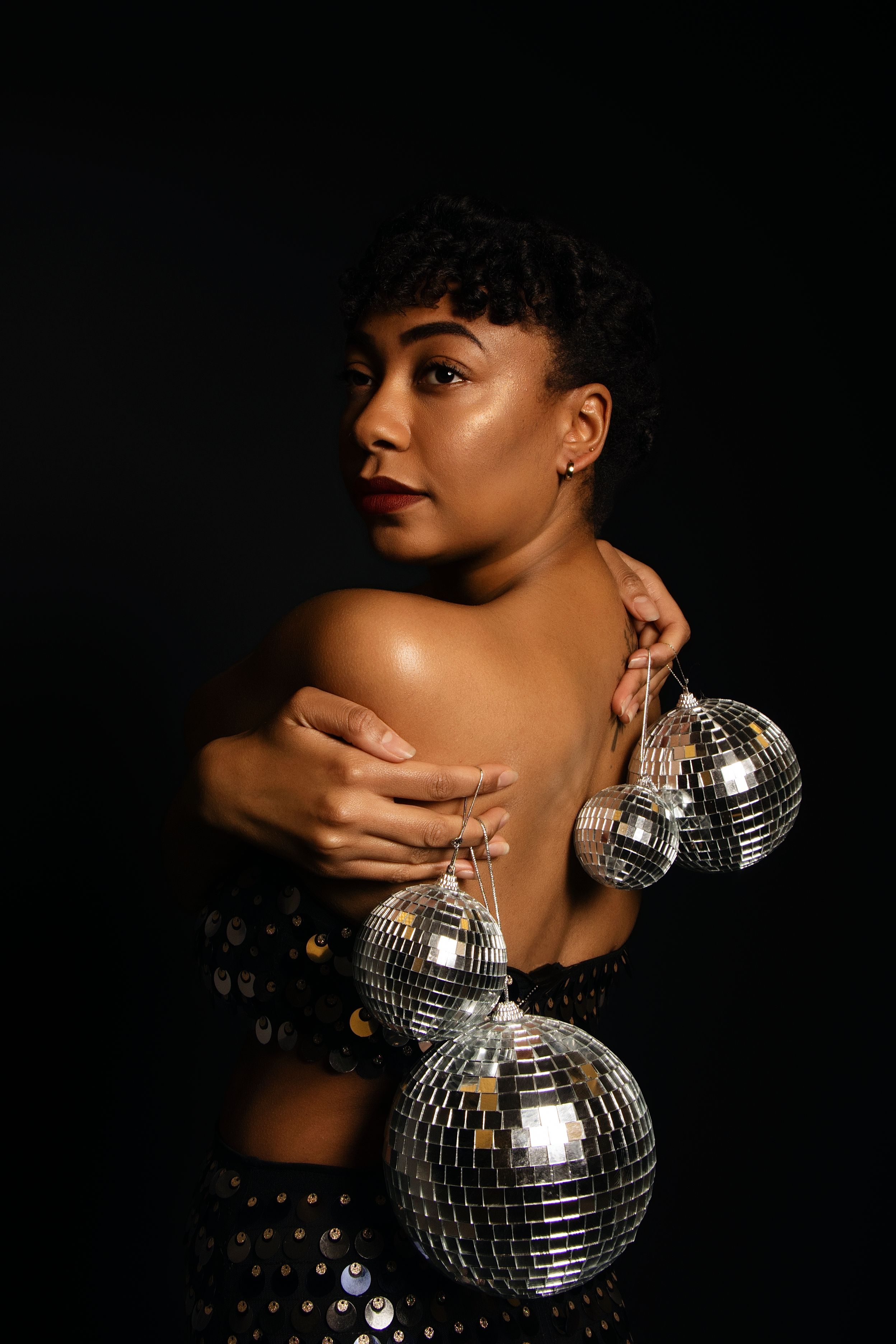 Close-up portrait with disco ball and sequined outfit in dramatic lighting.