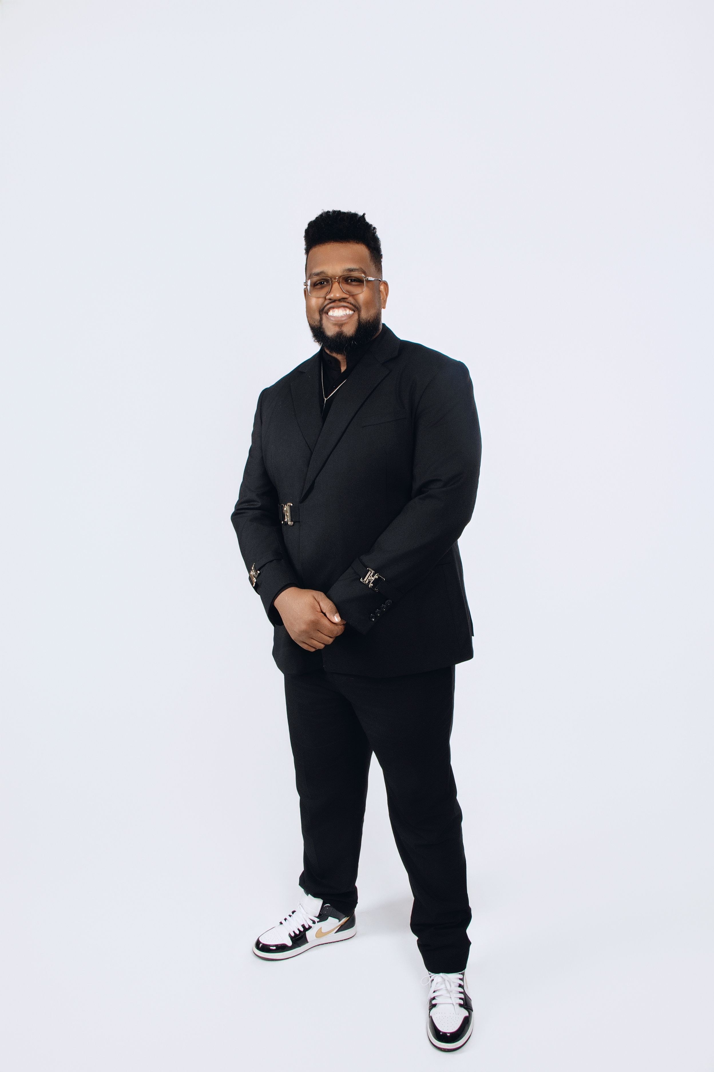 Stylish all-black outfit portrait session with sneakers against white studio backdrop.
