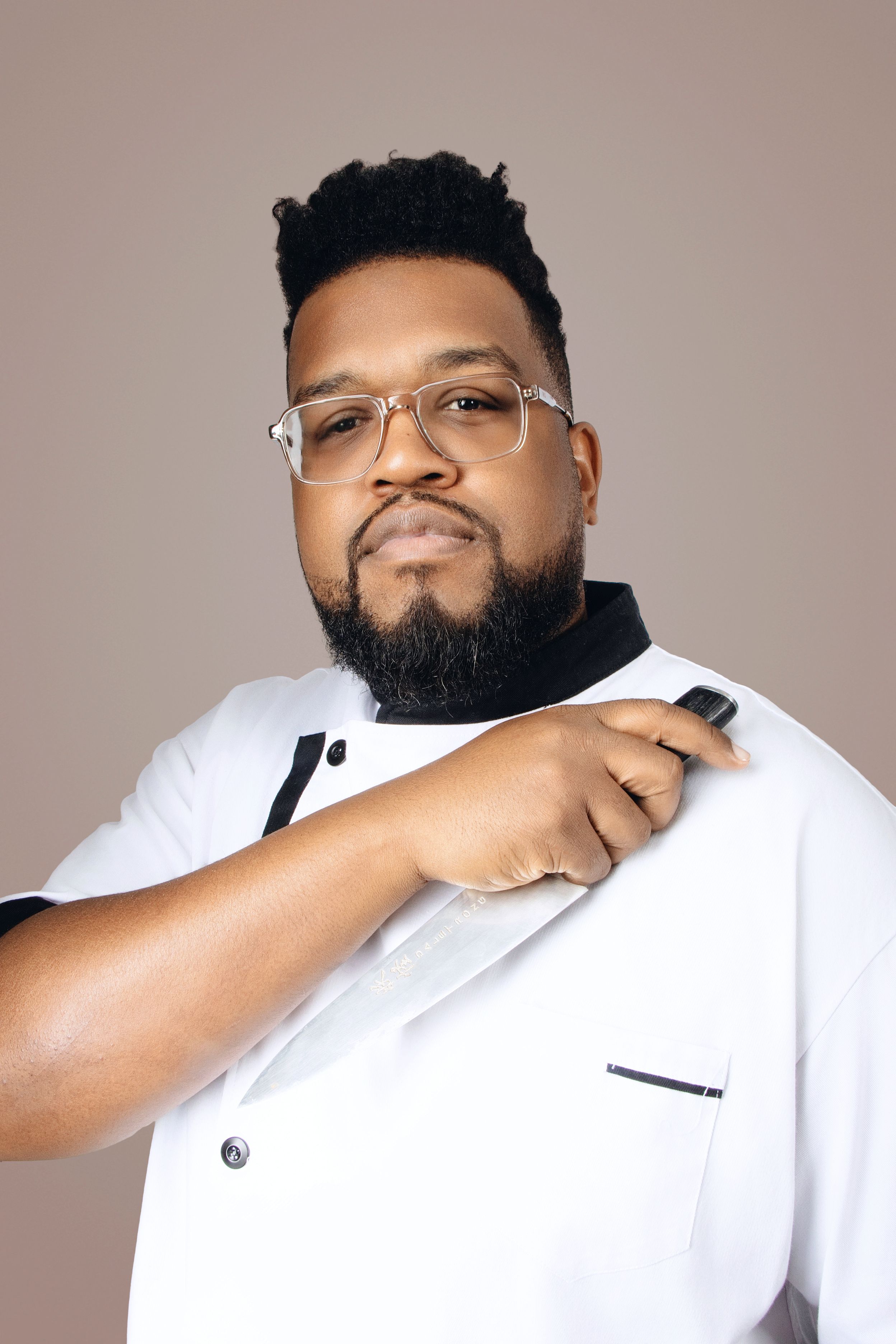 Close-up portrait in white chef coat showing playful expression against neutral background.