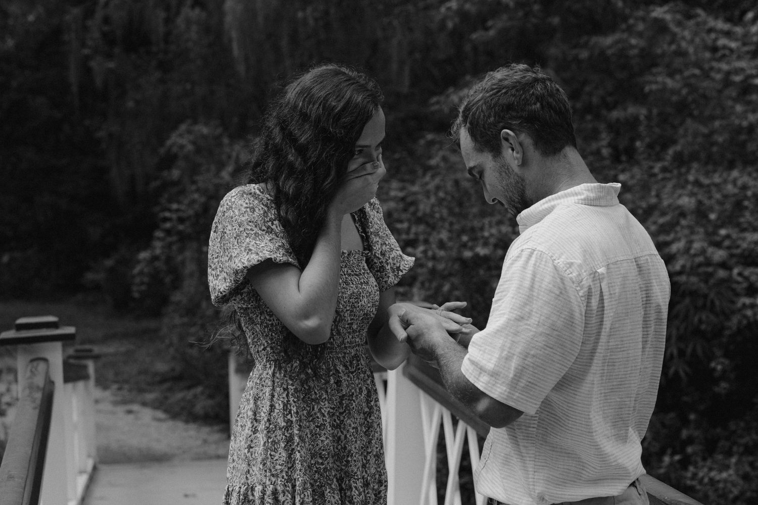 A couple shares an emotional moment on a bridge during what appears to be a proposal.