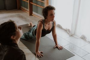 A person performs a plank exercise on a yoga mat in a bright, minimalist room with tiled flooring.