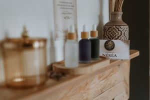 Decorative glass bottle with ornate pattern sits on wooden shelf alongside other beauty products in soft focus.