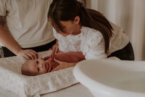 A tender moment during a baby's diaper change on a soft white changing pad.
