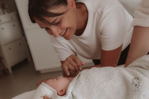 Parent and baby share a joyful moment together while laying on white bedding in a cozy bedroom.