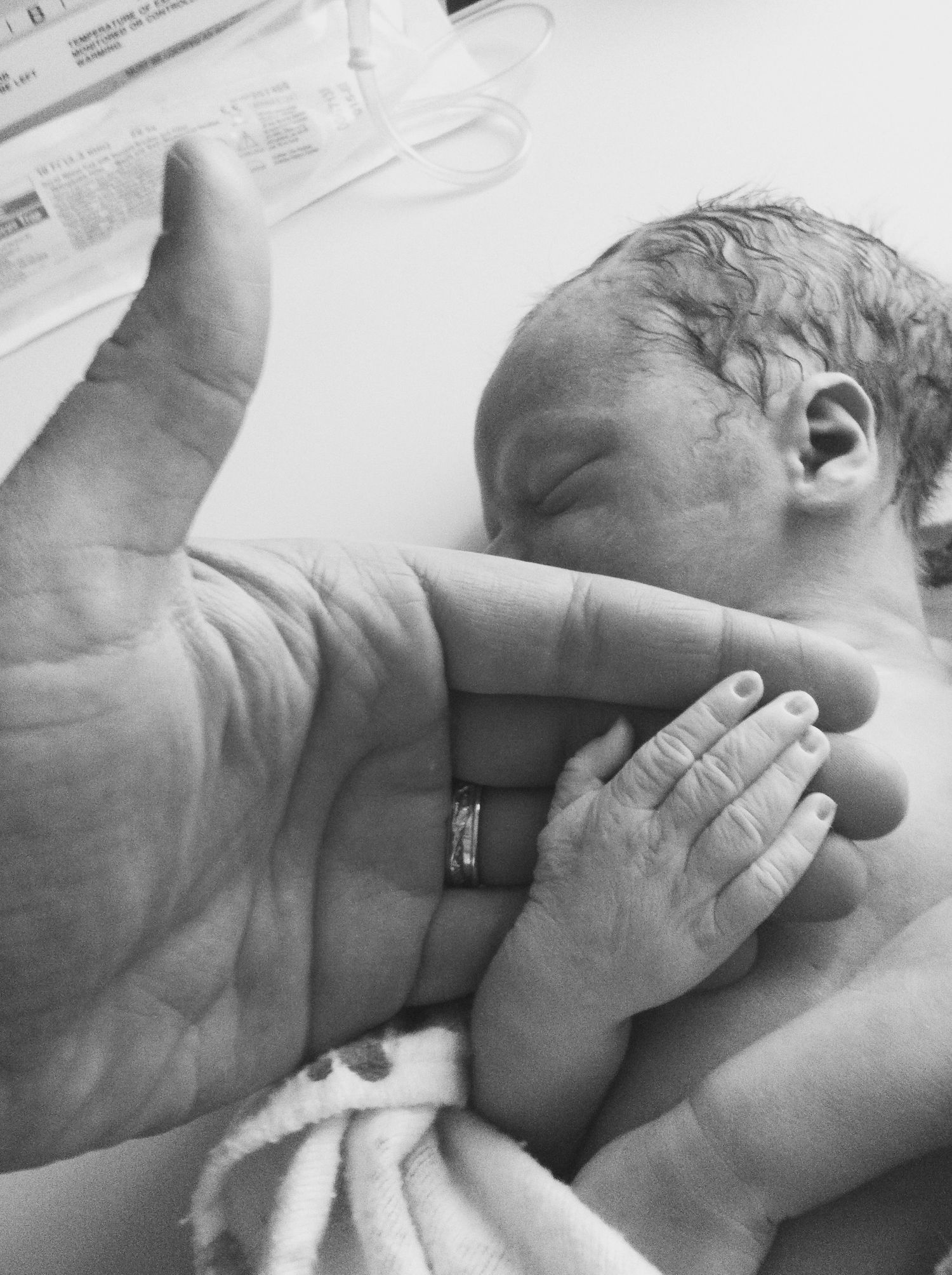 Black and white close-up of newborn baby's hand grasping an adult finger.