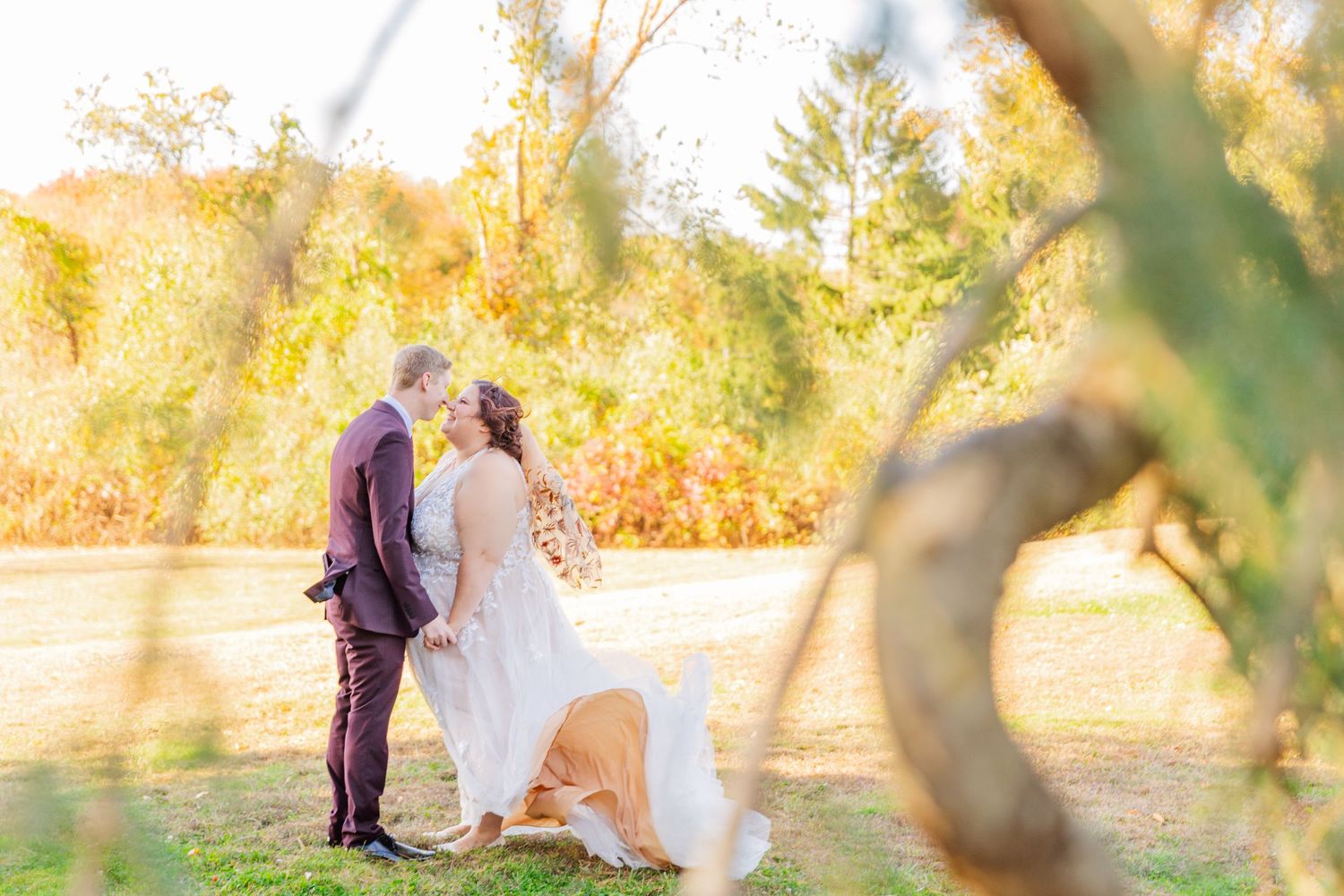 Couple in wedding attire embracing in sunlit garden with autumn foliage.