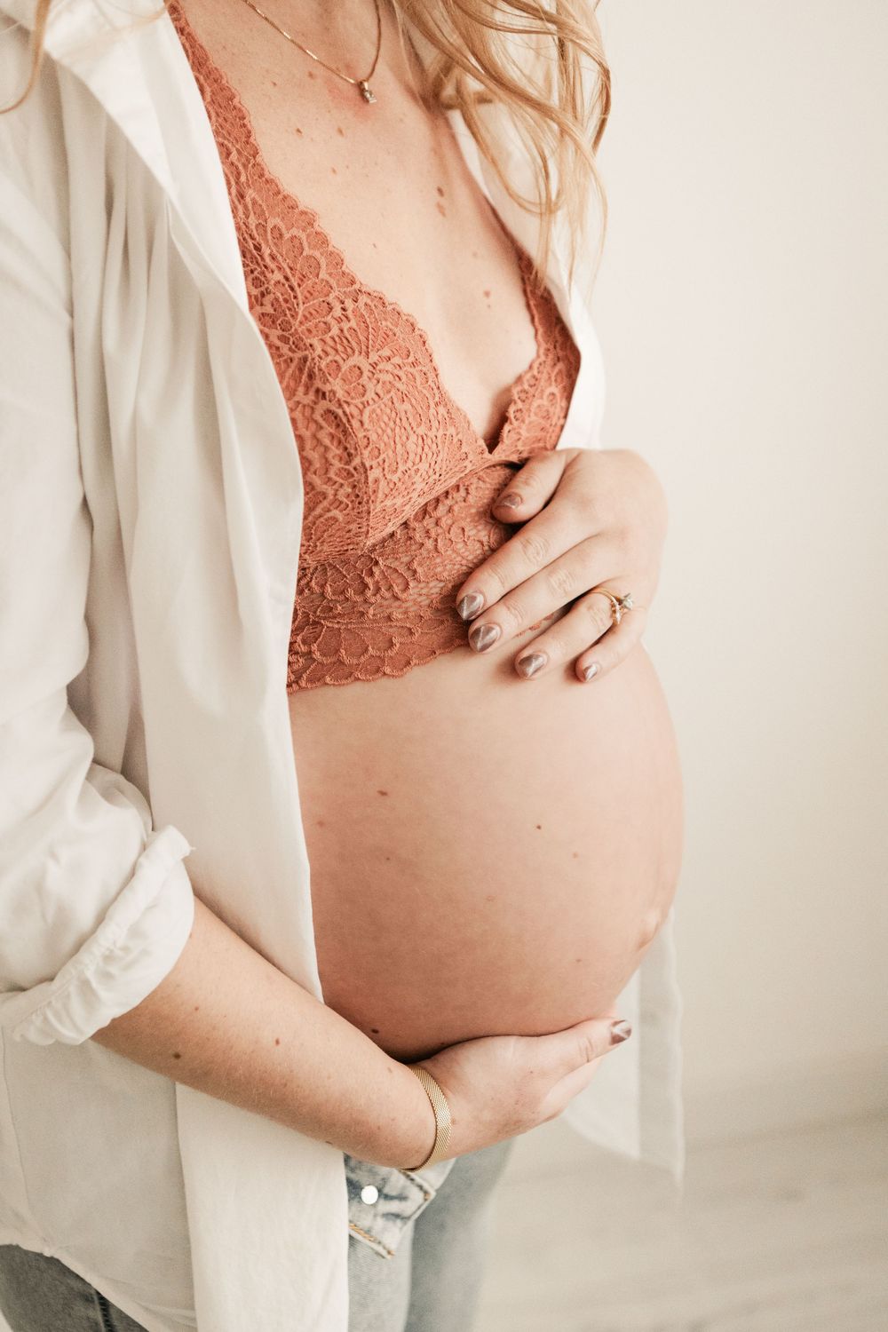 Pregnant woman in lace bralette and white shirt cradling baby bump, maternity photography.Cornwall Maternity Photographer