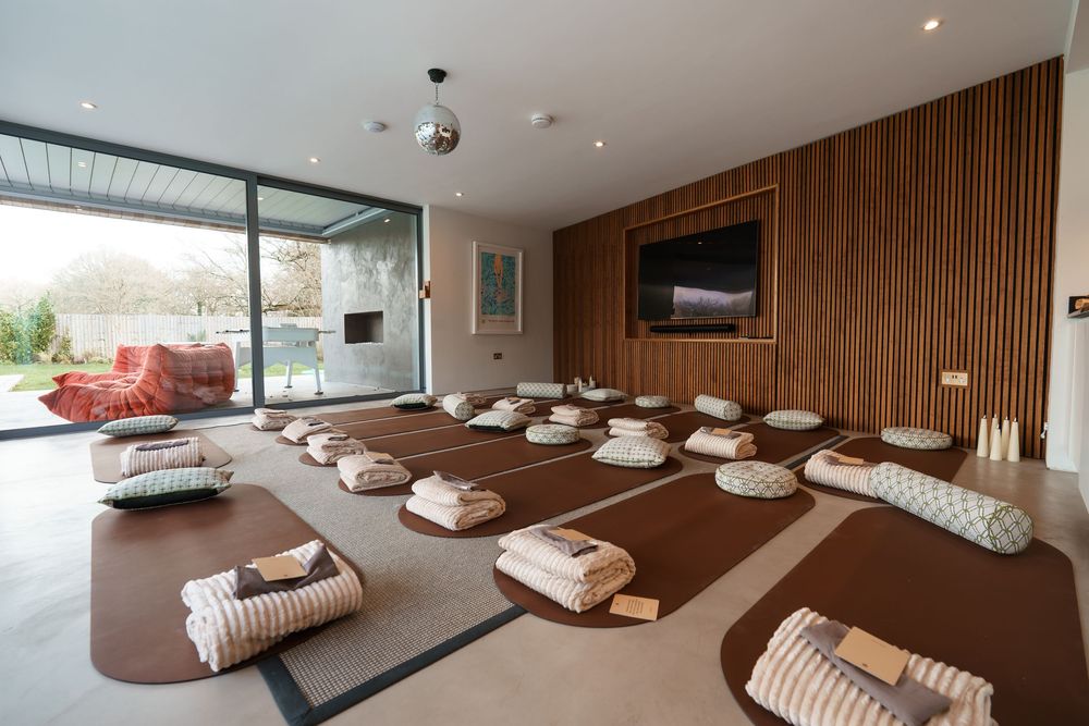 Serene meditation room with cushioned mats, wooden walls, and large glass doors opening to a garden.