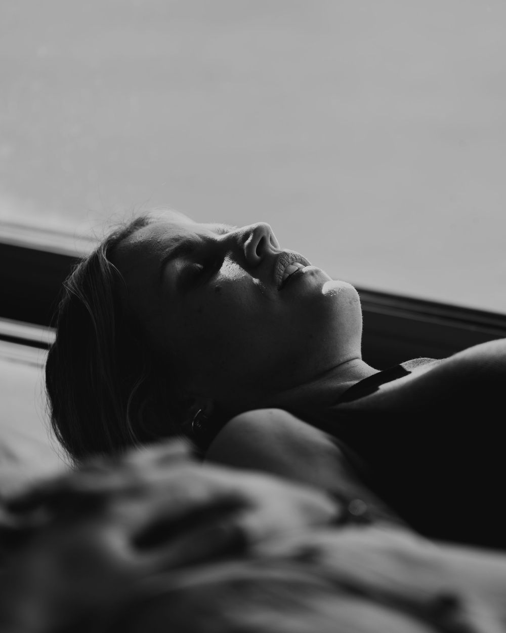 Black and white portrait of a woman reclining with head tilted back, captured in dramatic low-key lighting.