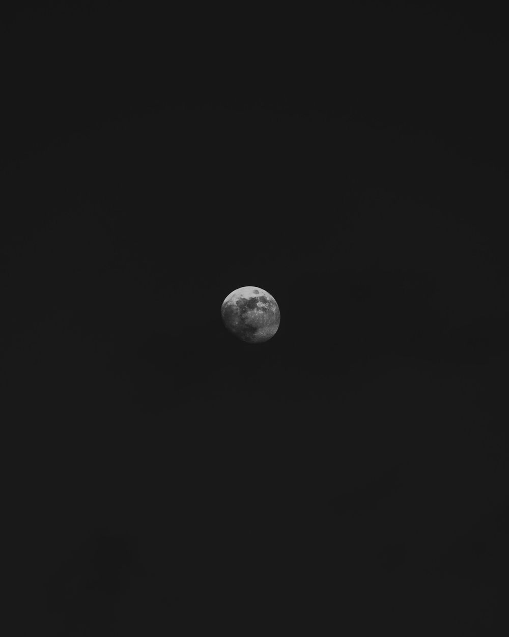 A nearly full moon glows against a dark night sky in this minimalist black and white photograph.