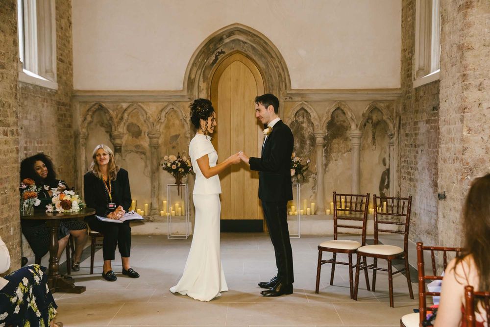 Couple exchanging vows at an elegant stone chapel wedding ceremony with guests seated nearby.
