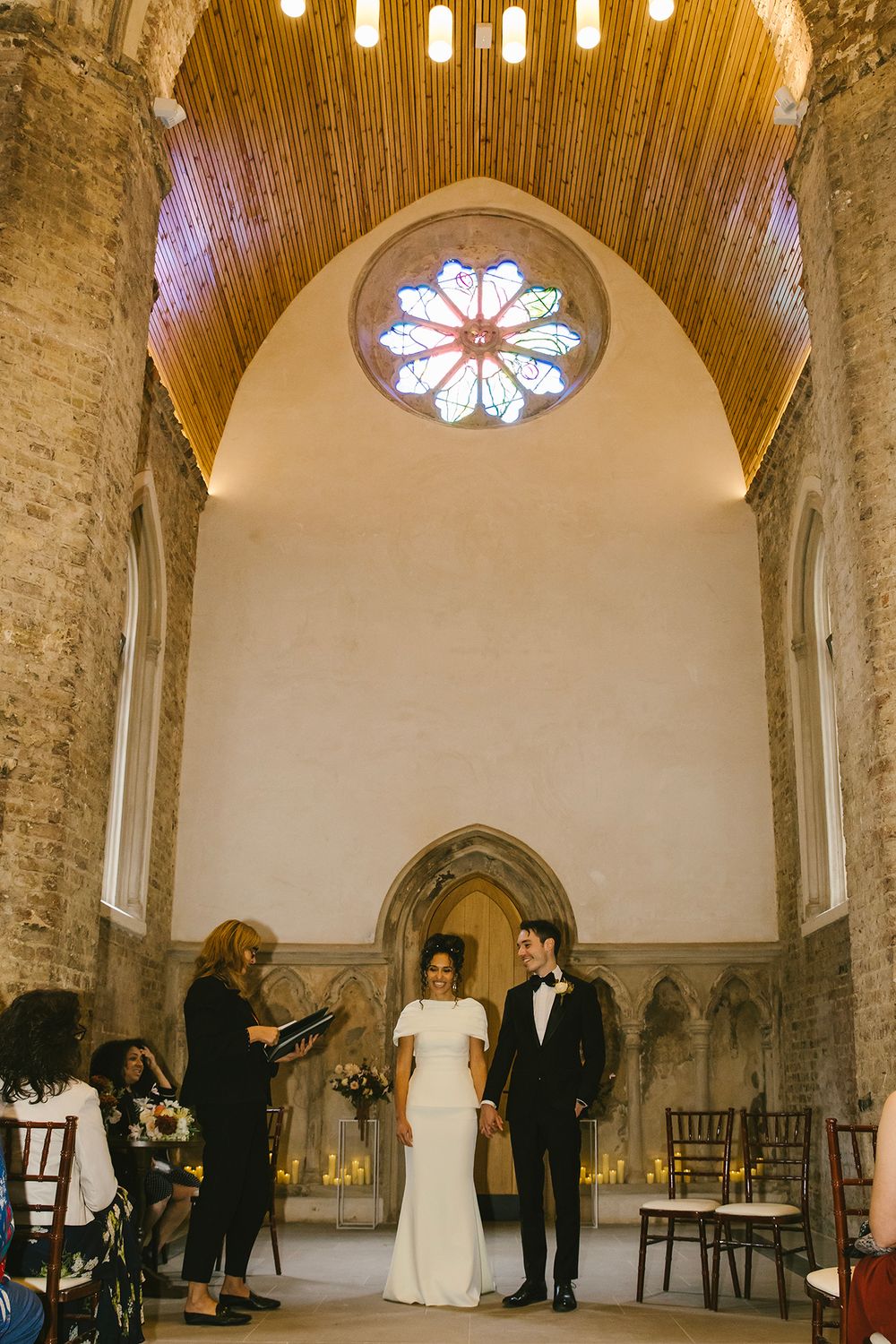 Bride and groom exchange vows in a stunning Gothic chapel with arched ceilings, stained glass rose window, and candlelit altar.
