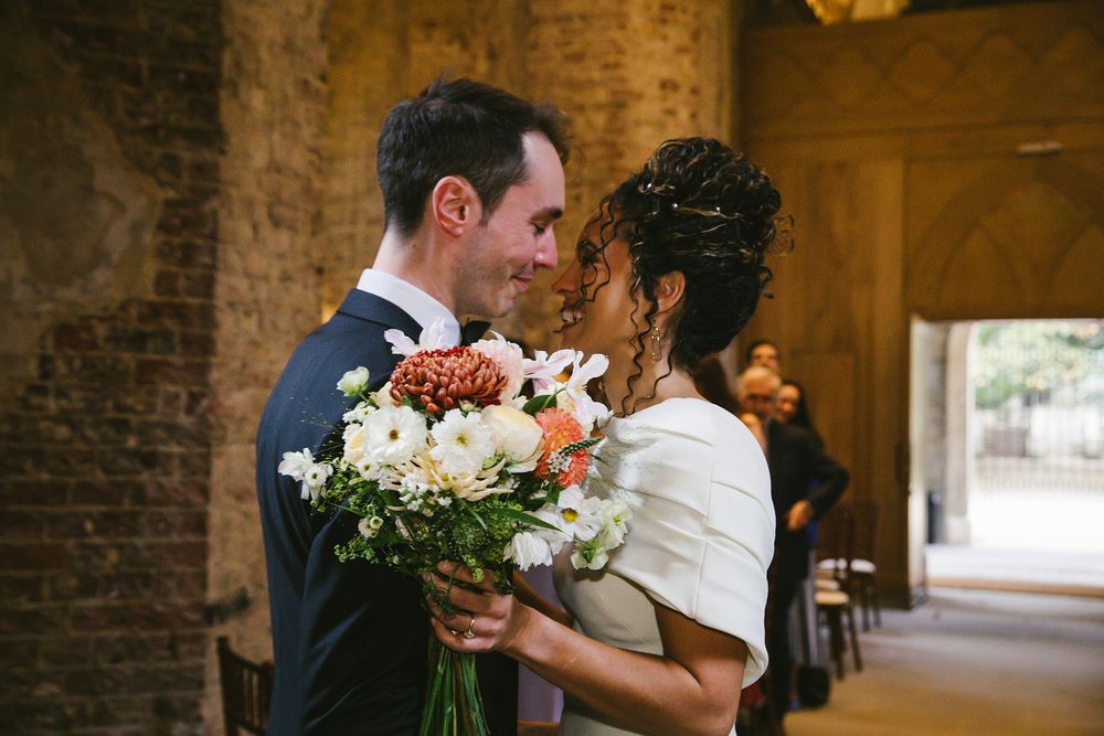 Bride and groom share a romantic moment holding a colorful bouquet in a rustic brick venue.