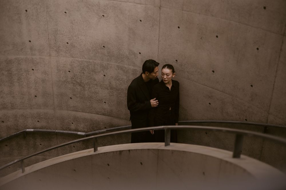 A couple shares a tender moment together on a curved concrete staircase with a metal railing.