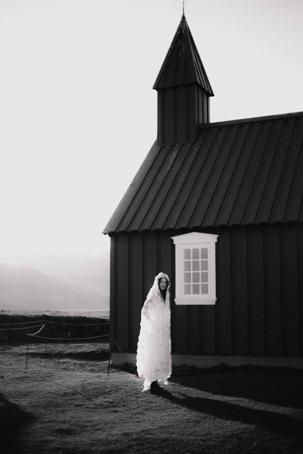 Black Nordic church silhouetted against white sky with flowing white fabric in foreground.